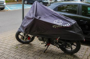 Cobblestone Caddesi 'ne park etmiş, koruyucu siyah su geçirmez kapaklı motorlu scooter.