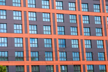 Mavi Gök Altında Geometrik Pencere Desenli Modern Turuncu ve Gri Apartman Cephesi