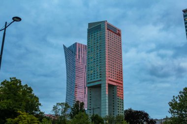Şehir manzarasında Pembe ve Yeşil Cepheli Modern İkili Gökdelenler Dramatik Bulutlu Gökyüzüne Karşı