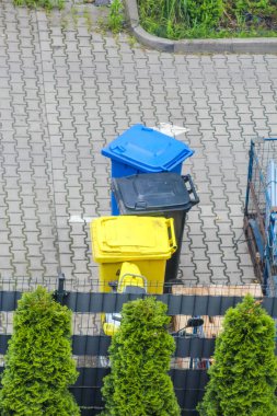 Mavi ve Sarı Konteynırlı Renkli Geri Dönüşüm Kutuları Paved yüzeyinde Yeşil Çitler