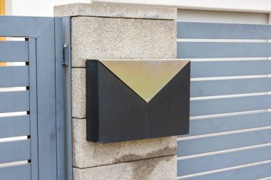 Çağdaş çitlere monte edilmiş siyah ve altın üçgen desenli modern geometrik tasarım posta kutusu