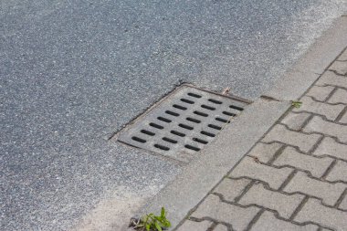 Asfalta gömülü sokak tahliye ızgarası ve bitişik beton kaldırım kenar altyapı detaylarını gösteriyor