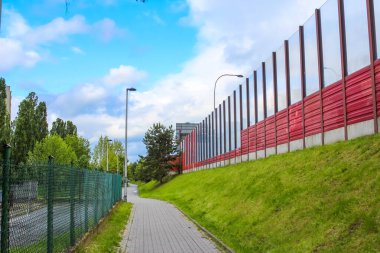 Yeşil tepe boyunca uzanan modern Kırmızı Ses Duvarı Şehir Altyapısı Oluşturuyor