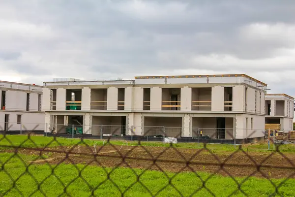 Bitmemiş modern apartman kompleksi inşaatı bulutlu bir günde tel örgülerin arkasından görülüyor.