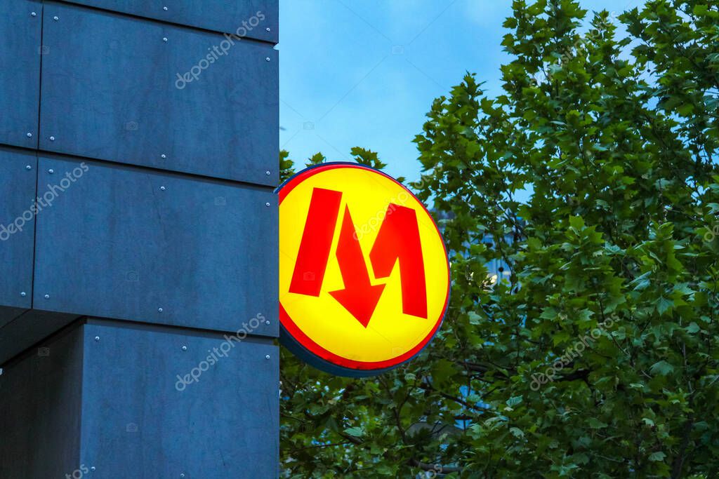 Bright Yellow Metro Sign with Red M Symbol Against Blue Sky and Green Trees