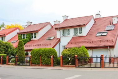 Kırmızı kiremit çatılı, beyaz cepheli, küçük ön bahçeli ve güvenlik çitli ev sıraları.