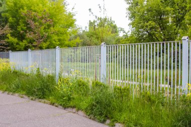 Yeşil Bahar Çimeni ve Çalıları ile Banliyö Geçidi boyunca Modern Metal Dikey Çit