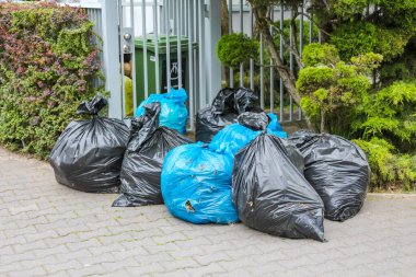 Siyah ve Mavi Çöp Torbaları Dekoratif Bahçe Bitkileri ve Beyaz Çit Yakınlarında Toplandı