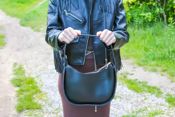 Deri ceketli bir adam, bahar yeşiliyle çevrili taşra çakıl yolunda siyah bir çanta taşıyor.