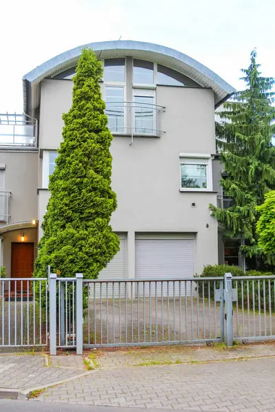 Yüksek konik yeşil ağaç ve banliyö yerleşim yerlerinde metal çit kapısı olan modern kemerli çatı.