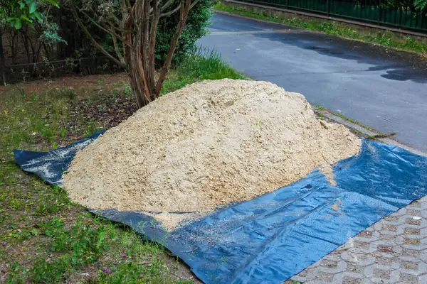Dışarıdaki inşaat projesi için çimenli alanda mavi muşambayla kaplanmış inşaat kumu yığını.