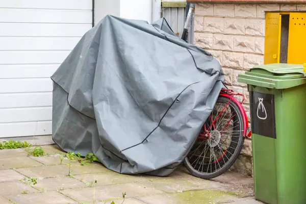 Bisikletler Gri branda ile kaplı Yeşil Çöp Kutusunun yanında Beyaz Duvara Karşı