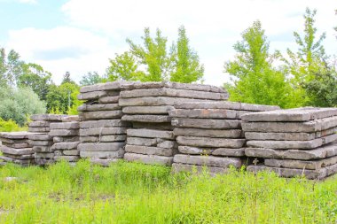 Arka planda yemyeşil ağaçlar olan çimenli bir arazide yığılmış beton bloklar endüstriyel bir manzara yaratıyor.,