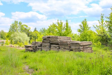 Tüylü beyaz bulutlar ile berrak mavi bir gökyüzünün altında yeşil çimlerin üzerinde uzanan eski ahşap kirişlerin bulunduğu doğal bir manzara terk edilme veya inşaat sürecinde olduğunu gösteriyor.,