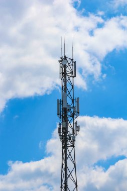 Beyaz kabarık bulutlu parlak mavi gökyüzüne karşı çoklu antenli modern hücresel iletişim kulesi