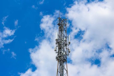 Uzun iletişim kulesi kabarık beyaz bulutlarla mavi gökyüzüne doğru uzanıyor.