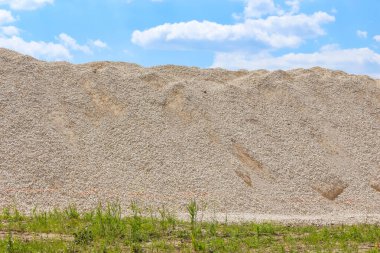 Geniş kum yığını inşaat alanı boyunca yeşil çimen ön plan kontrastı ile genişliyor