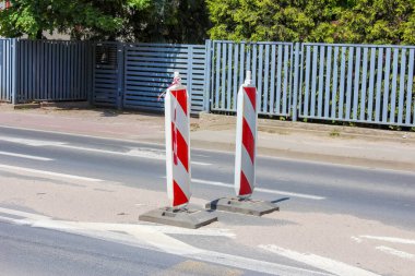 Metal çitin yakınındaki beton kaldırıma yerleştirilmiş beyaz ve kırmızı çizgili trafik kolları