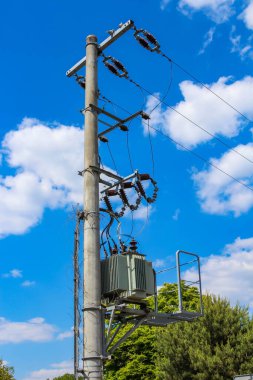 Uzun, yıpranmış bir elektrik direği. Sayısız elektrik hattı ve elektrik teçhizatı. Açık mavi gökyüzü, seyrek bulutlar, kentsel altyapı ve bağlantıyı temsil ediyor.,