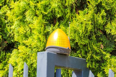 Gri bir direkte parlak sarı bir sinyal ışığı veya lamba, canlı yeşil bir yeşillik zemin üzerine kurulmuş, olası bir uyarı veya rehberlik göstergesi,