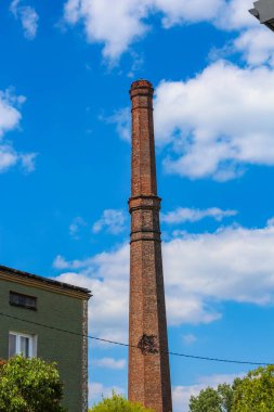 Uzun, yıpranmış bir tuğla baca ya da endüstriyel yığının parlak mavi gökyüzüne karşı yükselmesi birkaç bulutla endüstriyi, dayanıklılığı ya da tarihi bir simgeyi sembolize eder.,