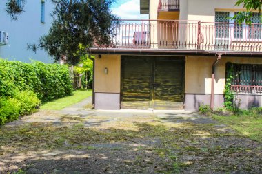 Kahverengi çatılı ve açık renkli duvarları olan iki katlı büyüleyici bir ev, yeşil ağaçların arasına kurulmuş ve bakımlı bir çimenlik, sakin bir banliyö evini tasvir ediyor.,