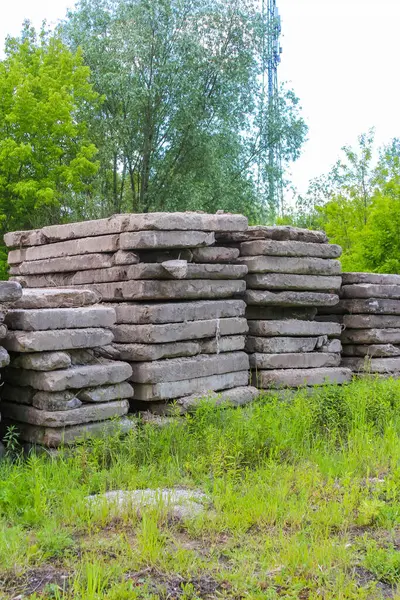 Yıpranmış beton bloklar, yemyeşil ağaçların yanında çimenli bir yamaçta duruyor ve ham endüstriyel bir manzara yaratıyor.,
