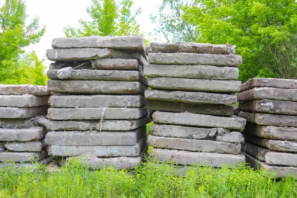 Geniş, yıpranmış beton bloklar parlak bir gökyüzünün altında canlı yeşil bir çimenlikte duruyor. Yeni amaçlanan yapı malzemelerini sergiliyorlar.,