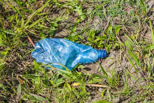 Çöpe atılmış bir mavi plastik torba kuru yeşil çimenler ve kahverengi yaprakların üzerinde uzanıyor. Çevresel kirliliği ve insan doğası üzerindeki insan etkisini vurguluyor.,