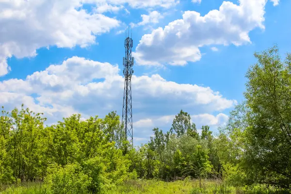 Doğadaki teknolojiyi temsil eden, dağınık beyaz bulutlarla dolu, canlı mavi gökyüzü altında, yemyeşil ağaçların üzerinde iki hücresel iletişim kulesi yükseliyor.,