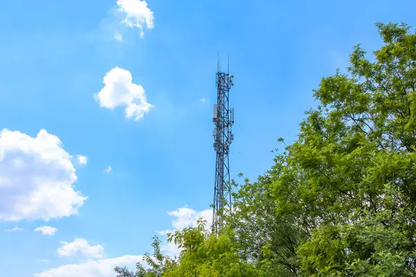 Kırsal alanda tüylü beyaz bulutlarla parlak mavi gökyüzüne karşı duran uzun iletişim kulesi.