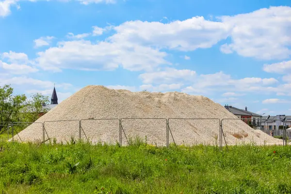 Büyük kum yığını, beyaz bulutlu açık mavi gökyüzü altında endüstriyel alana hakim.