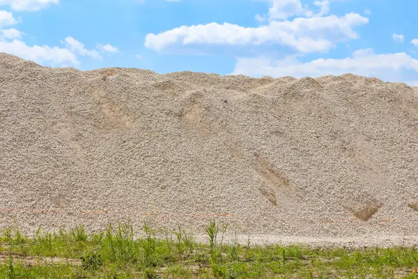 Geniş kum yığını inşaat alanı boyunca yeşil çimen ön plan kontrastı ile genişliyor
