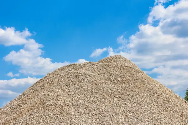 Muazzam konik kum yığını mükemmel geometrik dağ şekilleri yaratıyor. Yumuşak bulutlu parlak mavi gökyüzüne karşı.