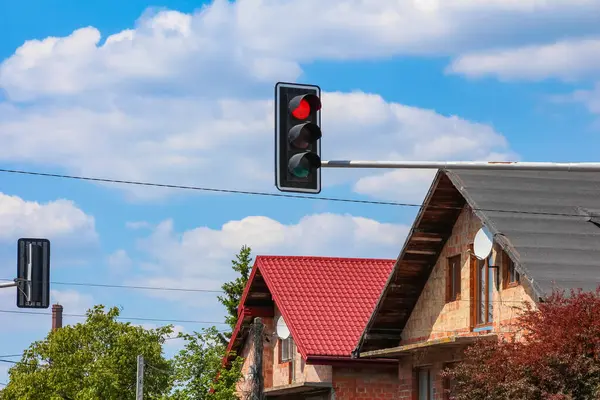 Kırmızı kiremit çatılı geleneksel ev ve yeşil ağaçlı mavi gökyüzüne bakan trafik ışığı