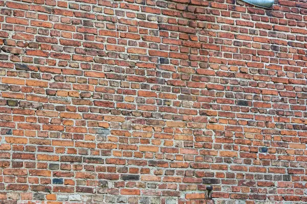 Geleneksel kırmızı tuğla duvar dokusu, çeşitli tonlarda yıpranmış yüzeyi ve doğal yaşlanma düzenini açık havada gösteriyor.