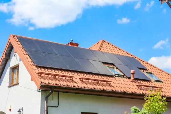 Kırmızı kiremit çatılı ve beyaz duvarlı modern mesken evleri. Parlak mavi gökyüzünün altında bulutlu güneş panelleri var.