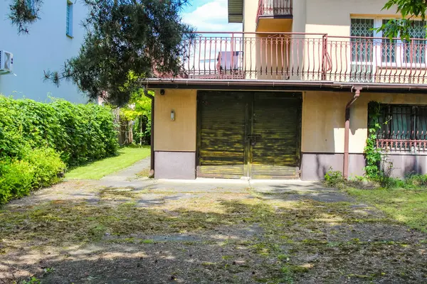 Kahverengi çatılı ve açık renkli duvarları olan iki katlı büyüleyici bir ev, yeşil ağaçların arasına kurulmuş ve bakımlı bir çimenlik, sakin bir banliyö evini tasvir ediyor.,