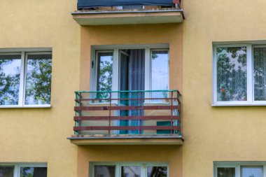 Mavi balkon korkulukları ve Avrupa tarzında beyaz pencere çerçeveleri olan sarı bina cephesi
