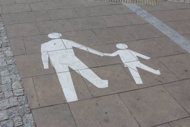 Elele tutuşan yetişkin ve çocuk figürlerini gösteren beton kaldırımda beyaz boyanmış yaya geçidi sembolleri