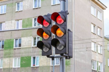 Trafik ışığı direğe monte edilmiş kırmızı ve sarı sinyalleri gösteriyor ve yerleşim binası şehir arka planında.