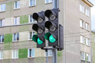 Trafik lambası gündüz trafik kontrolü sırasında arka planda görünen kentsel apartman binaları ile yeşil sinyali gösteriyor