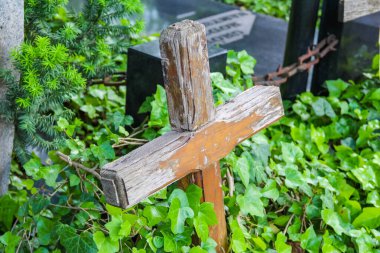 Kırsal ahşap bir haç, muhtemelen bir mezar taşı, yemyeşil bitki örtüsünün ortasında, metal bir zincir ile dikiliyor..