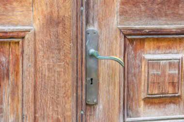 Eski, yıpranmış, metal saplı ve oyulmuş aksanlı ahşap bir kapının detaylı bir yakın çekimi..