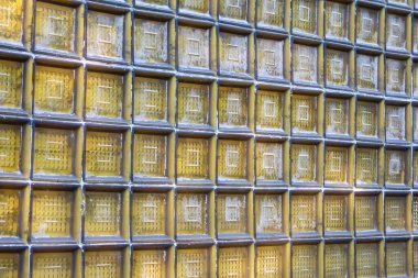 Şeffaf cam blok bir duvar yakın çekim ızgara deseni ile, soyut bir arkaplan dokusu oluşturur sıcak, altın renkli.