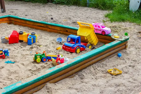 Oyun zamanı boyunca yeşil kenarlı kum havuzuna saçılmış renkli plastik oyuncaklar