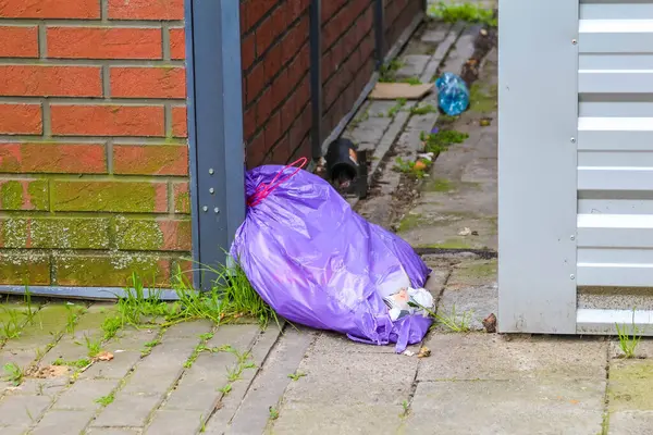 Mor çöp torbası ve döküntüler yerleşim yerinin girişinin yanındaki asfalt zemine bırakılmış.