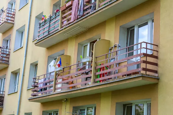 Beyaz balkon korkulukları ve pencerelerinde çiçek kutuları olan çok katlı sarı bir apartman.