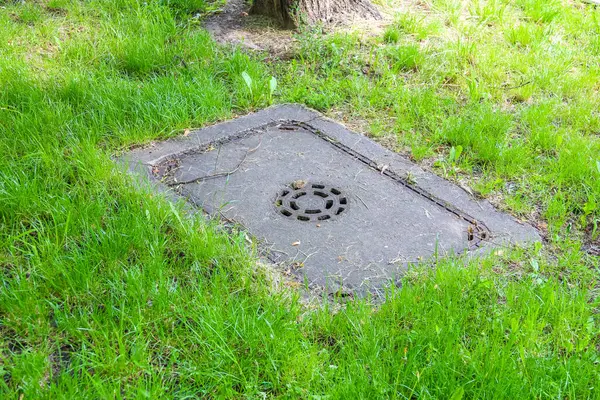 Canlı yeşil çimlere gömülü geometrik desenli kare beton drenaj kapağı