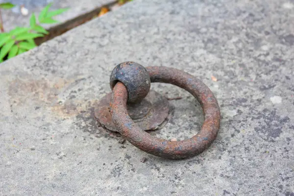 Yıpranmış beton yüzeye gömülü ağır demir halka yaş ve aşınma belirtileri gösteriyor.